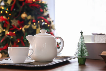 Cup, teapot with hot beverage and Christmas decor on table