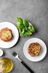 Plates with zucchini pancakes and herbs on grey table