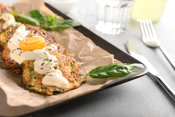 Tasty zucchini pancakes with sauce on plate