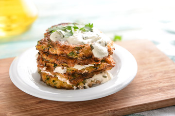 Plate with zucchini pancakes and sauce on wooden board