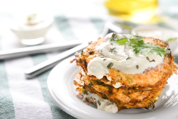 Tasty zucchini pancakes with sauce on plate