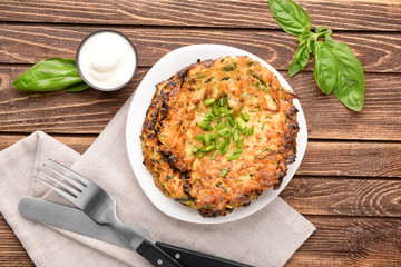 Plate with zucchini pancakes and sauce on wooden table