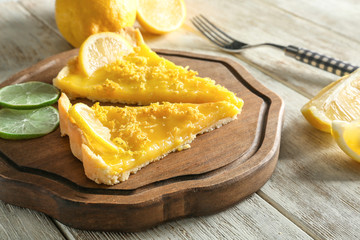 Board with pieces of delicious lemon pie on wooden table