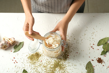 Woman taking homemade sauerkraut from jar with spoon at white table