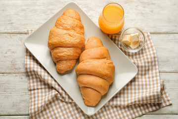 Plate with tasty croissants and glass of orange juice on wooden table