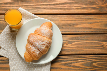 Plate with tasty croissant and glass of orange juice on wooden table