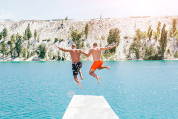 Gay men couple jumping in blue lake.