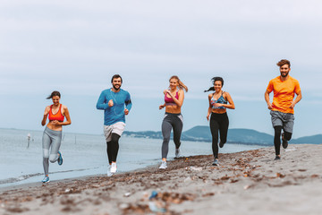 Group of young sports people running on the beach by the sea
