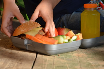 Cute schoolboy eating outdoors the school from plastick lunch boxe. Healthy school breakfast for child. Food for lunch, with sandwiches, fruits, vegetables (carrots cucumber tomato) , and juice