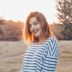 Young woman relaxing in summer sunset sky. Portrait of Beautiful Young Woman Backlit at Sunset Outdoors. Soft warm sunny colors.