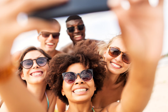 friendship, summer holidays and people concept - group of happy friends taking picture by smartphone on beach