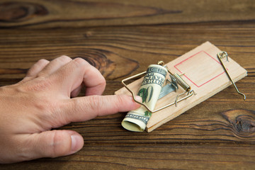 A man's hand got caught in a mousetrap with bait money dollar bills. Concept business risk, pimat...