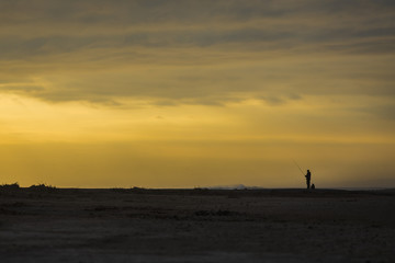 Naklejka na ściany i meble One fishermen man in contrast with the sunset sky at Lluta river wetlands on the beach area facing the Pacific Ocean just an amazing view, Arica, Chile