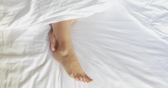 female legs in bed view from above, white bedding, 4k