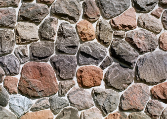 Assorted rocks of different sizes and colors embedded in concrete on an exterior rock wall
