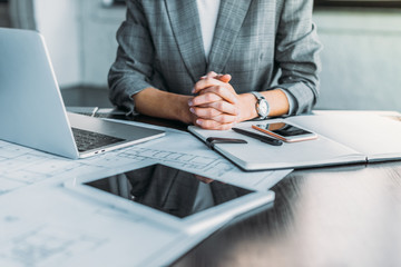 Fototapeta premium cropped image of businesswoman sitting at table in office with digital devices on tabletop