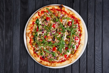 Top view of pizza with sausage, ham, olives, arugula, onion and tomato