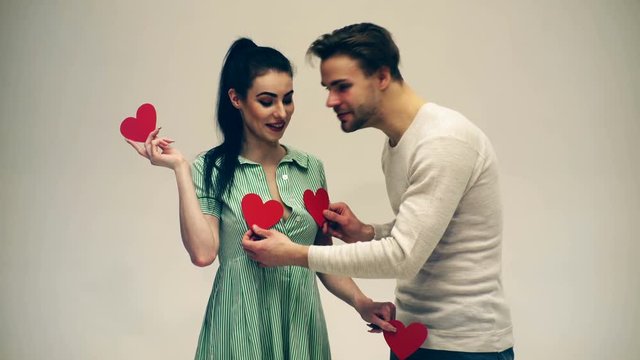 The guy closes the girl's chest with two hearts on a white background. A guy with a girl are kissing on Valentine's day. Valentine's day concept.