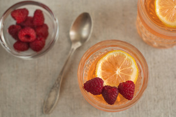 Cup with raspberries, spoon and glasses bowl filled with orange color jelly. Top view