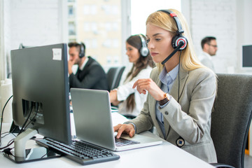 Pensive blonde businesswoman with headset working on laptop in call center