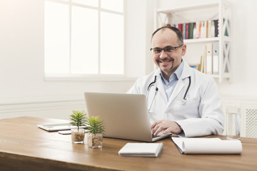 Naklejka na ściany i meble Portrait of doctor in glasses sitting at desktop