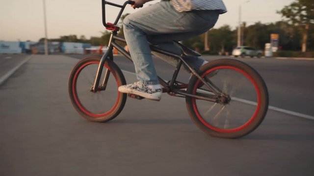 The bicyclist rides on his bmx outdoors at sunset. Slow motion close-up