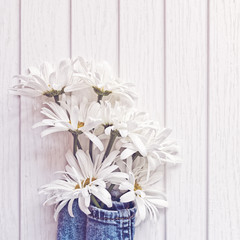 Obraz premium A bouquet of seven white daisies is wrapped in denim fabric. On the petals of flowers there are droplets of water. White wooden background.