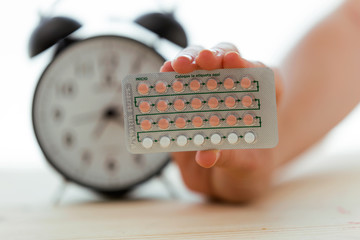 Contraceptive pills in hand witch clock over white background. Prevention concept.