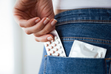 Woman with contraceptive pills and condom in the pocket of blue jeans.