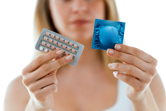 Beautiful woman showing condom and contraceptive pills over white background.