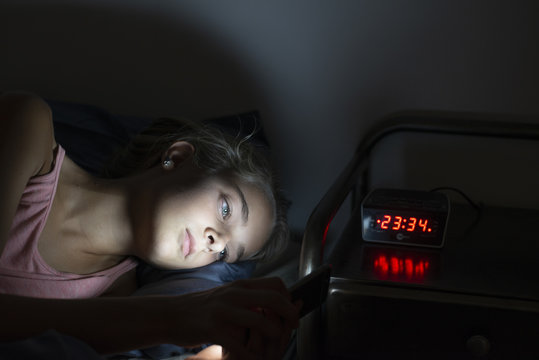 young girl using smartphone in bed at night. Mobile addiction.