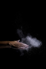 A woman beats her hands together, and white flour fly through the air. The shutter speed has been very fast. Image includes a effect.