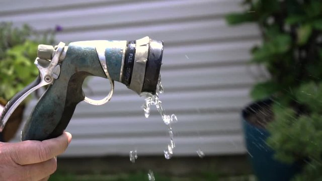 Hose nozzle spraying water close up, in slow motion