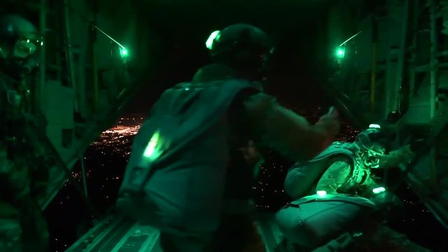 Paratroopers jump from a plane at night, in night vision.