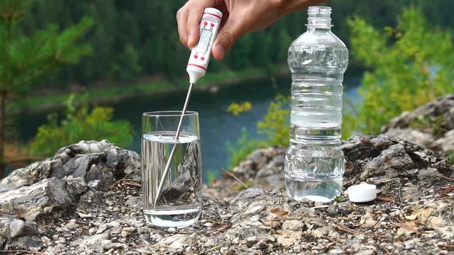 Man produces temperature measurement in Fahrenheit in glass of water, on mountainous area. Health and ecology slowmotion