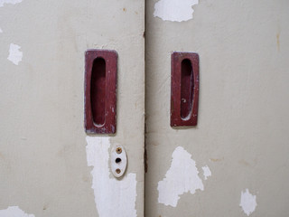Close-up of keyhole and flush door handles on an old closet with paint peels. Buildings and architecture.
