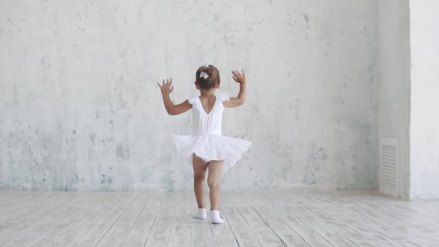a small ballerina in a white pack jumps up. slow motion. back view