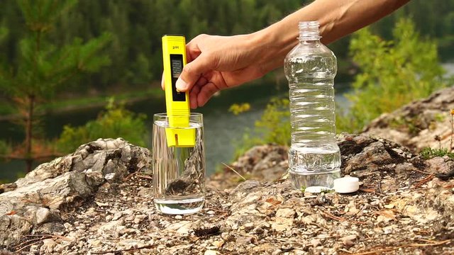 Man turn ON the appliance PH-meter in glass of water on mountain area. Theme of health and ecology. Slowmotion