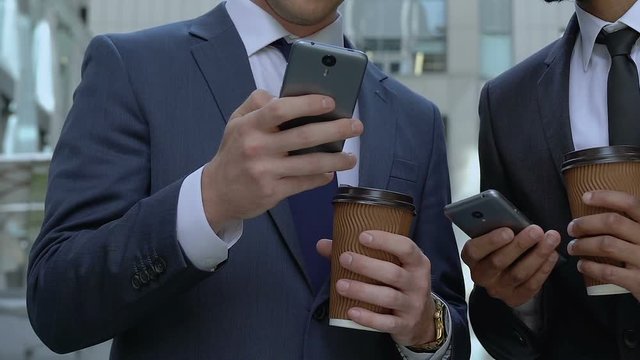 Businessmen at coffee break share photos on smartphone, impressions from holiday