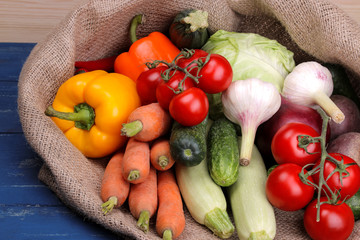 Fresh vegetables including garlic cucumbers cabbage onion pepper beetroot carrot zucchini and tomatoes in a bag on a blue wooden table