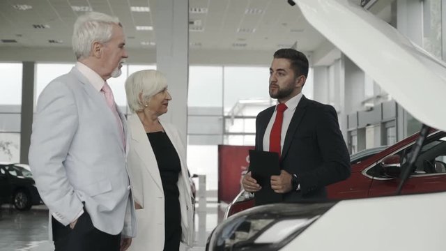 Sales assistent at the car salon is helping a senior couple to make a right choice.