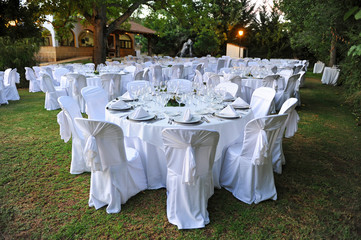 Mesas preparadas en blanco para la celebración de un banquete de bodas en un jardín al aire libre al atardecer