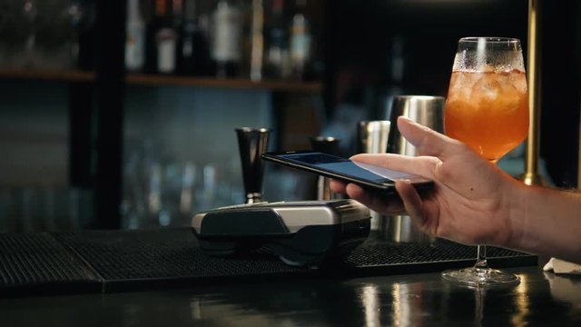 Close-up of woman making payment through NFC in bakery, cafe restaurant bar for cocktail lemonade, mobile phone contactless pay for bill with terminal, banking