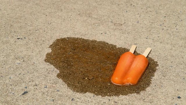 Orange double stick popsicle  dropped on a driveway melts with copy space