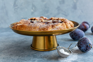 Homemade plum pie on a bronze stand.