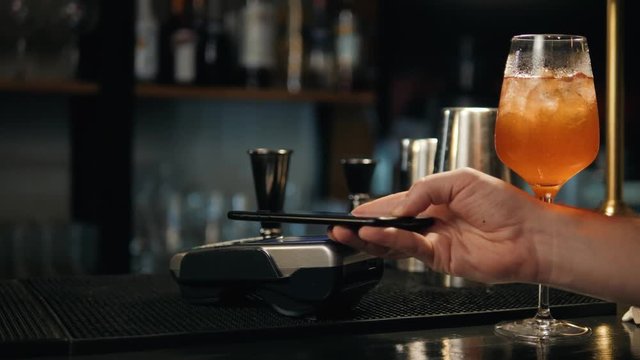 Close-up of woman making payment through NFC in bakery, cafe restaurant bar for cocktail lemonade, mobile phone contactless pay for bill with terminal, banking