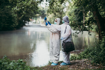 Two scientists in protective suits taking water samples from the river.