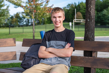 Happy teenager sitting on wooden bench that is next to a soccer/football field.