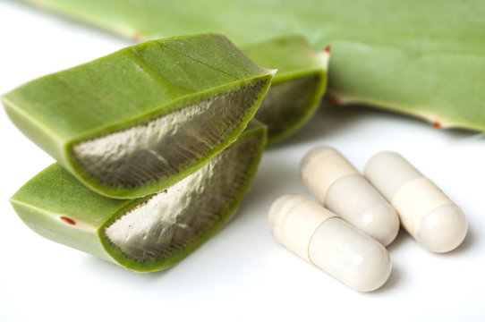 closeup of sliced aloe vera leaves and pills on white background