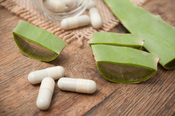closeup of sliced aloe vera leaves and pills on wooden background